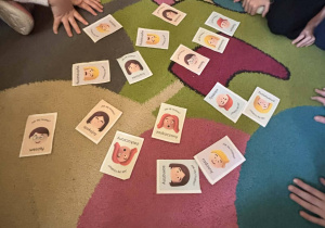 Karty z różnymi emocjami rozłożone na dywanie podczas zajęć w świetlicy.