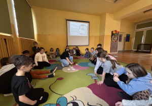 Uczniowie siedzą w kręgu na dywanie w świetlicy podczas zajęć o emocjach i depresji.