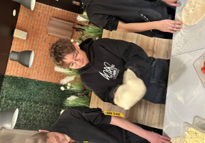 Uczeń klasy VIIa podrzuca i rozciąga ciasto na pizzę podczas warsztatów.