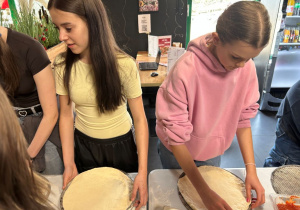 Uczennice klasy VIIa przygotowują ciasto do pizzy podczas warsztatów kulinarnych.