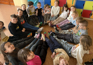 Dzieci siedzą w kręgu i pokazują kolorowe, niepasujące do siebie skarpetki jako symbol solidarności.