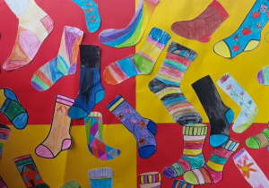 Kolorowe rysunki skarpetek wykonane przez uczniów, ułożone na tle czerwono-żółtej planszy.