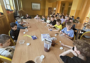 Dzieci siedzą przy stołach i wykonują prace podczas zajęć w świetlicy.