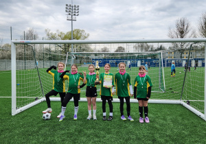Zwycięska drużyna dziewcząt SP 13 Pabianice z pucharem i dyplomem na boisku piłkarskim.