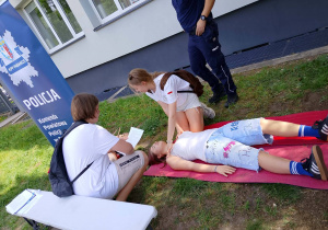 Uczniowie ćwiczą udzielanie pierwszej pomocy na macie pod okiem dorosłych.