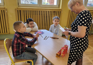 Nauczycielka stoi przy stoliku i sprawdza pracę uczniów podczas konkursu.