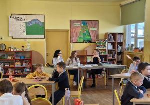 Uczniowie siedzą przy stolikach, a nauczyciele obserwują przebieg konkursu matematycznego.
