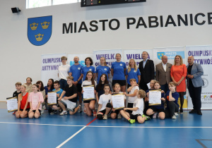 Duża grupa uczestników wydarzenia sportowego pozuje do zdjęcia w hali.