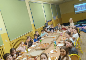 Dzieci jedzą pizzę przy stole podczas nocowania w szkole.