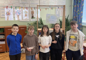 Grupa uczniów stoi w klasie obok drewnianej scenki teatralnej przygotowanej na lekcję języka polskiego.