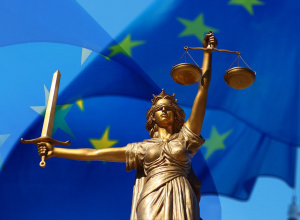 Powyższy obraz przedstawia klasyczną figurę Temidy — bogini sprawiedliwości — z mieczem w jednej ręce i wagą w drugiej, na tle flagi Unii Europejskiej.