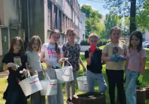 Grupa uczniów stoi obok szkolnych donic po zakończeniu prac ogrodniczych.