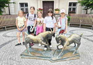 Uczniowie i nauczycielki podczas wycieczki do Poznania pozują do wspólnego zdjęcia przy rzeźbie poznańskich koziołków.