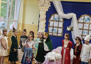 Uczniowie w kolorowych kostiumach występują na scenie podczas szkolnego spektaklu.