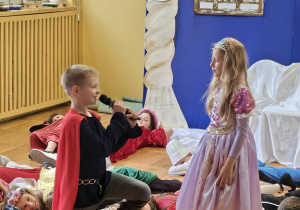 Uczeń w stroju księcia rozmawia z królewną podczas przedstawienia „Śpiąca Królewna”.