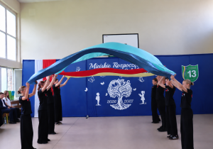 Występ szkolnego zespołu cheerleaderek podczas Miejskiego Rozpoczęcia Roku Szkolnego 2026/2027. Uczennice prezentują efektowny układ choreograficzny z wykorzystaniem dużych, kolorowych tkanin.