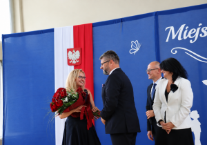 Dyrektor szkoły Anna Michalak odbiera bukiet kwiatów podczas Miejskiego Rozpoczęcia Roku Szkolnego 2026/2027. Towarzyszą jej przedstawiciele władz miasta.