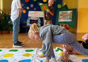 Dzieci bawią się na dużej macie w kolorowe kropki podczas szkolnych obchodów Dnia Kropki.