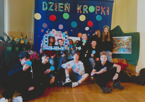 Grupa starszych uczniów pozuje na tle dekoracji z napisem „Dzień Kropki” i prezentacji Ogrodu Talentów.