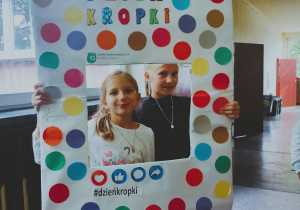 Dwie uczennice pozują do zdjęcia w kolorowej foto-ramce przygotowanej z okazji Dnia Kropki.