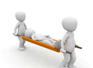 Trójwymiarowa ilustracja w stylu kreskówkowym. Dwie białe, bezosobowe postacie niosą na pomarańczowych noszach trzecią postać leżącą bez ruchu.