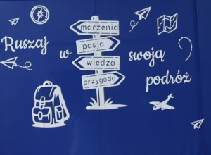 Dekoracja na niebieskim tle przedstawiająca biały napis: „Ruszaj w swoją podróż” oraz drogowskaz z kierunkami: „marzenia”, „pasja”, „wiedza”, „przygoda”.