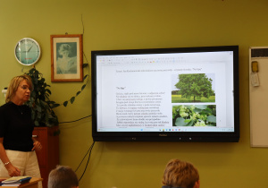 Nauczycielka języka polskiego, pani Małgorzata Krawczyk, prowadzi lekcję w klasie. Na tablicy interaktywnej wyświetlony jest temat: „Jan Kochanowski miłośnikiem ojczystej przyrody – czytamy fraszkę: ‘Na lipę’”, wraz z tekstem utworu i zdjęciami drzewa lipy. Na pierwszym planie widać ucznia, w tle roślina, zegar i portret dziewczynki czytającej książkę.