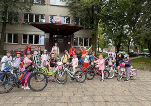 Klasa 2b z SP13 w Pabianicach z rowerami i w kaskach przed budynkiem szkoły. Grupa przygotowuje się do wycieczki rowerowej, w tle drzewa i szkolny budynek.