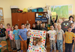 Klasa 2a świętuje Dzień Kropki – dzieci w ubraniach w grochy pozują z kolorową ramką i tabliczką „Wierzę w siebie”.