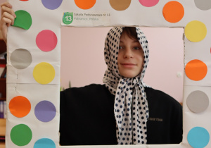 Uczeń Szkoły Podstawowej nr 13 w Pabianicach pozuje w ramce ozdobionej kolorowymi kropkami z napisem „Dzień Kropki”. Ma na głowie zawiązaną chustkę w czarne kropki.