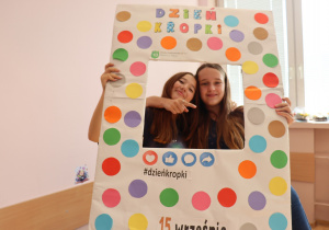 Dwie uczennice klasy 6a Szkoły Podstawowej nr 13 w Pabianicach pozują w kolorowej ramce z napisem „Dzień Kropki”, uśmiechnięte i przytulone.