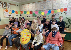 Uczniowie klasy 5b ze Szkoły Podstawowej nr 13 w Pabianicach pozują do wspólnego zdjęcia z okazji Dnia Kropki. Ubrani są w elementy ozdobione kropkami – chustki, opaski, ubrania. Na pierwszym planie widoczna „Kropka Mocy” – plakat z pozytywnymi hasłami.