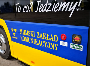 Napis na żółto-niebieskim autobusie MZK Pabianice: „To co? Jedziemy!” oraz „Miejski Zakład Komunikacyjny”. Widoczny przycisk i instrukcja otwierania drzwi.
