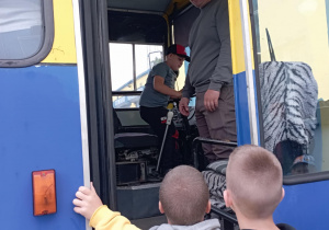 Uczeń klasy 2B wchodzi do kabiny kierowcy autobusu MZK w Pabianicach podczas wycieczki. Dzieci oglądają miejsce pracy kierowcy z bliska i słuchają wyjaśnień pracownika.
