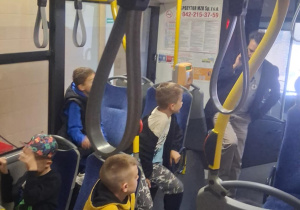Dzieci z klasy 2B SP13 słuchają opowieści pracownika MZK w autobusie. Edukacyjna wycieczka pozwala im poznać tajniki pracy kierowcy i funkcjonowanie komunikacji miejskiej.