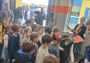 Dzieci z klasy 2B SP13 obserwują pokaz pracy wulkanizatora w MZK. Edukacyjna wycieczka pozwala im poznać zawody związane z komunikacją miejską i zaplecze techniczne.