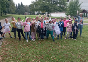 Grupa uczniów SP13 z nauczycielką pozuje na trawie podczas akcji Sprzątanie Świata – dzieci uśmiechają się i pokazują ręce w rękawiczkach, trzymając worki na śmieci.