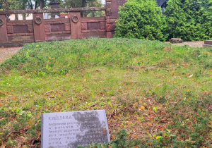 Kwatera grobowa rodziny Enderów na cmentarzu ewangelickim w Pabianicach, w tle rzeźba kobiety i czerwony pomnik, na przodzie czarna tablica z opisem.