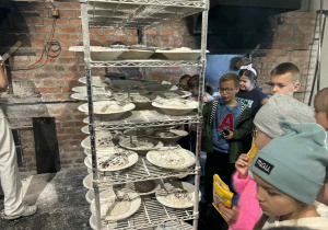 Uczniowie klasy 2A i 2B oglądają regał z ciastem chlebowym gotowym do wypieku w tradycyjnej piekarni z ceglanymi ścianami.