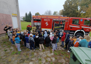 Grupa uczniów klasy II stoi przed otwartym wozem strażackim OSP Pabianice, słuchając strażaków prezentujących sprzęt ratowniczy.