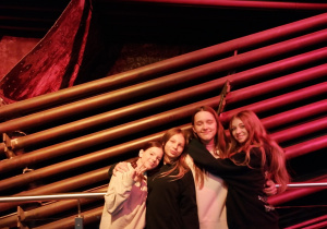 Uczennice pozują przy instalacji z rur w czerwonym świetle podczas wycieczki.