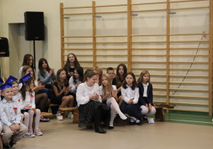 Uczniowie starszych klas obserwują ślubowanie pierwszoklasistów w sali gimnastycznej.