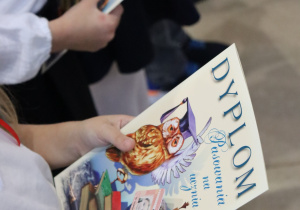 Uczeń trzyma dyplom pasowania na ucznia i legitymację szkolną.