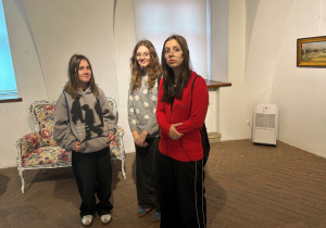 Trzy uczennice klasy 7a stoją w muzealnej sali podczas zwiedzania wystawy „Kisling w Pabianicach”. W tle widoczna stylizowana sofa w kwiatowy wzór oraz obrazy prezentowane na ścianach.