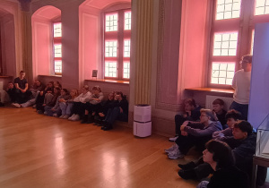 Grupa uczniów klasy 8b siedzących pod oknami w muzealnej sali, uczestniczących w lekcji o sztuce Kislinga.