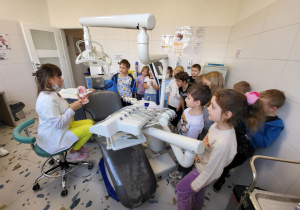 Uczniowie klasy 1b stoją przy fotelu dentystycznym i słuchają pani stomatolog.