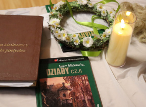 Książka „Dziady cz. II”, tom poezji Mickiewicza, zapalona świeca i wianek kwiatowy jako dekoracja wydarzenia literackiego.