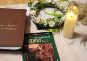 Książka „Dziady cz. II”, tom poezji Mickiewicza, zapalona świeca i wianek kwiatowy jako dekoracja wydarzenia literackiego.