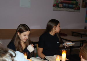 Ala i Iga z klasy 7a biorą udział w wieczornym czytaniu „Dziadów”, siedząc przy stole oświetlonym świecami.