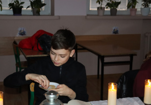 Peter z klasy 7b siedzi przy świecach podczas czytania „Dziadów” i trzyma talerzyk z ziarnami jako element obrzędu.